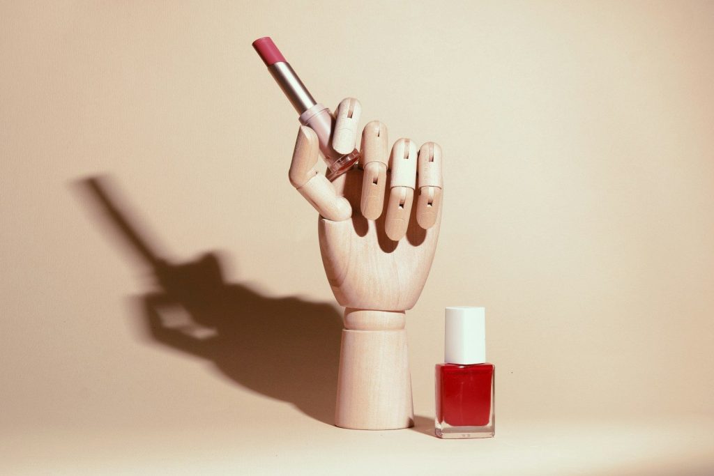 Wooden hand holding lipstick next to nail polish